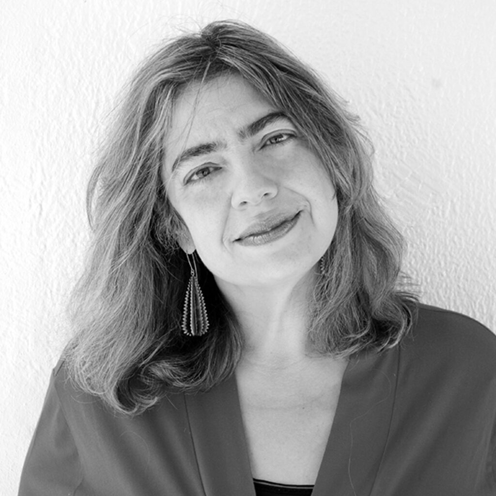 Black and white portrait of Esther Solomon, a woman with shoulder-length hair, wearing a pair of statement earrings and a relaxed, gentle smile, in front of a light-colored background.