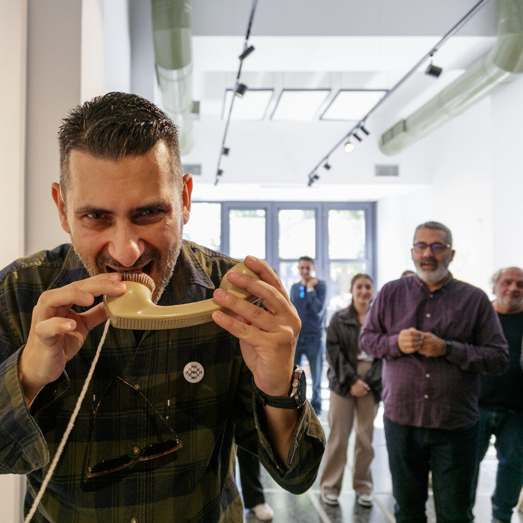 A person from the guided tour audience engages with a participatory installation biting a small muffin, while other visitors watch and smile.