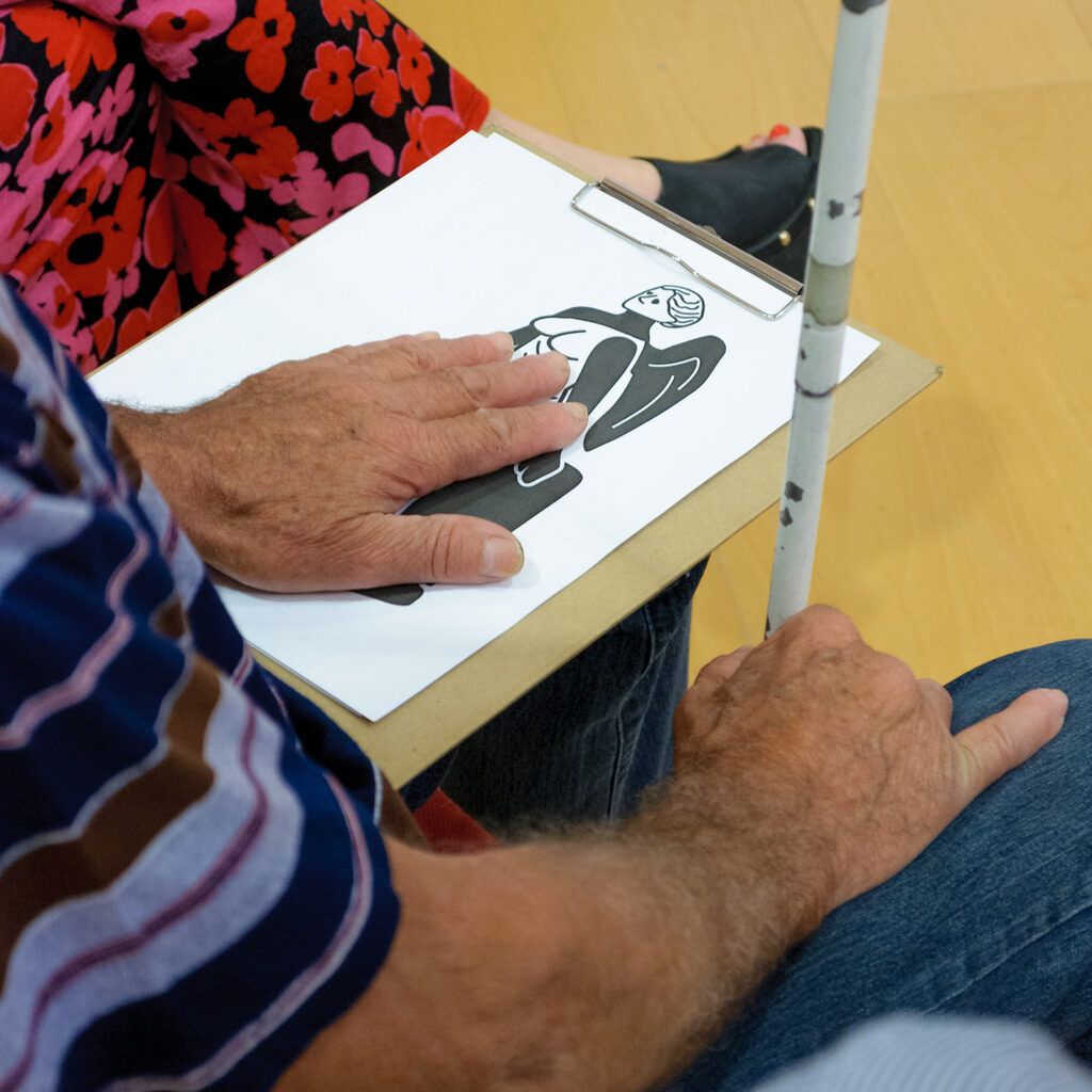 Άνδρας αγγίζει μια απτική αναπαράσταση του έργου με το ένα χέρι ενώ με το άλλο κρατάει το λευκό μπαστούνι του