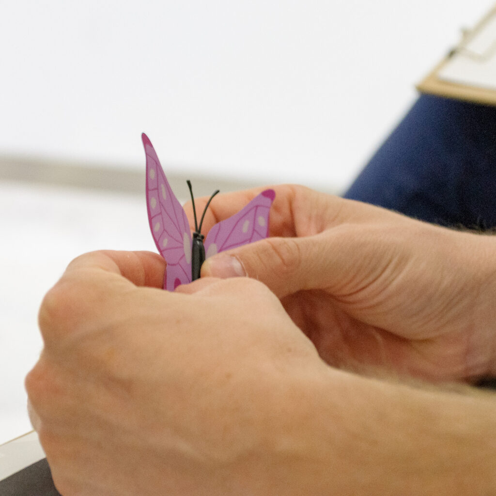 Hands holding a lilac plastic butterfly.