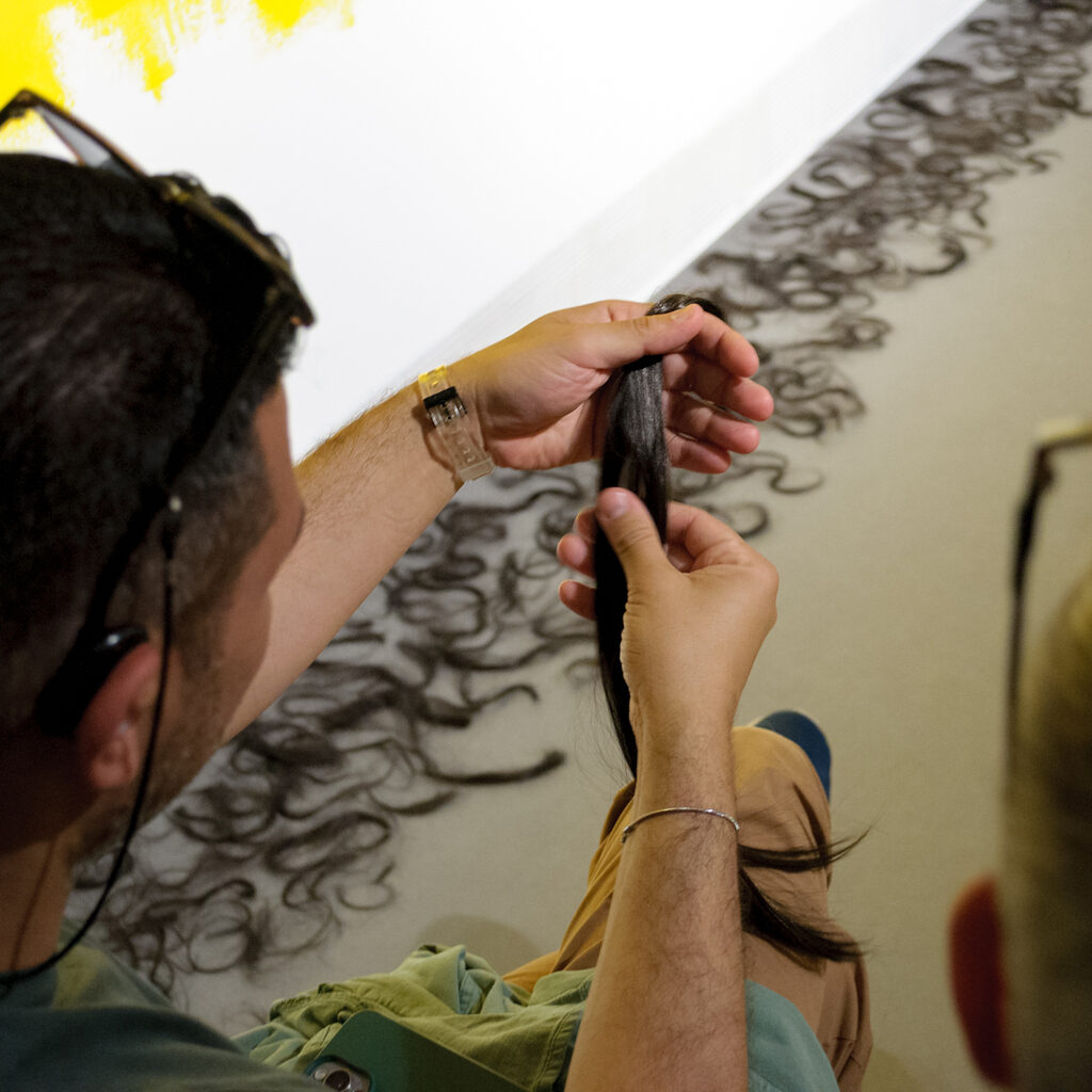 Man touching a lock of black hair while other locks of hair from the installation can be seen on the floor
