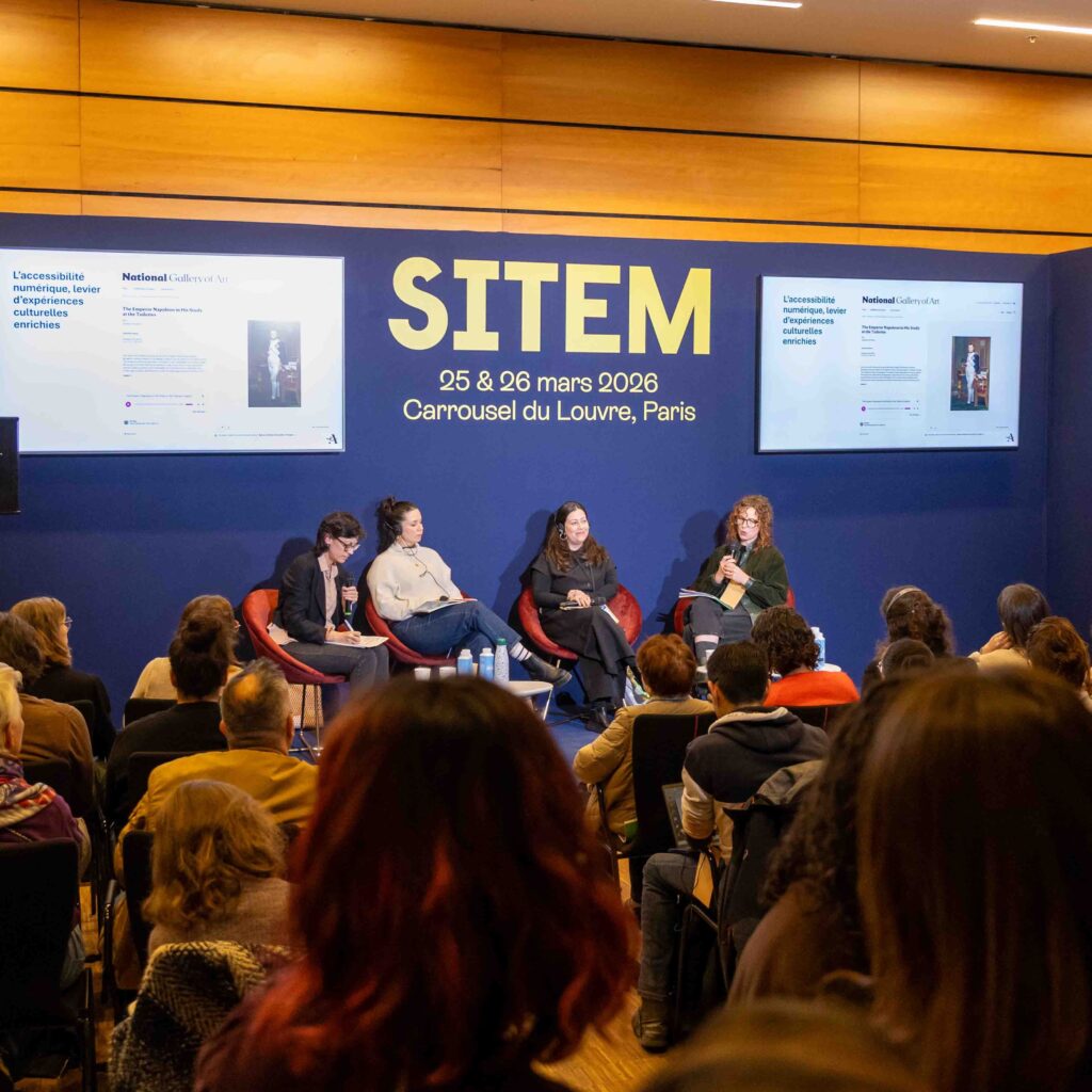 Wide view of the panel room at SITEM 2026 in Paris. Two screens display content about accessibility in culture, while four speakers discuss in front of an audience.