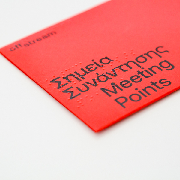 Close-up of the red envelope containing a Meeting Points 2025 postcard, featuring the bilingual title in print and embossed Braille.