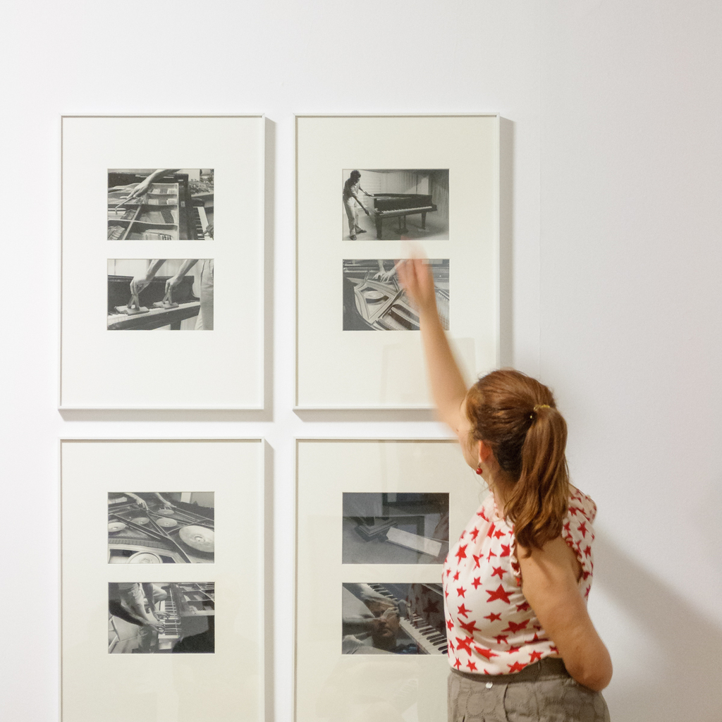 A woman with red hair in ponytail is pointing at a black n white photograph in a museum space.